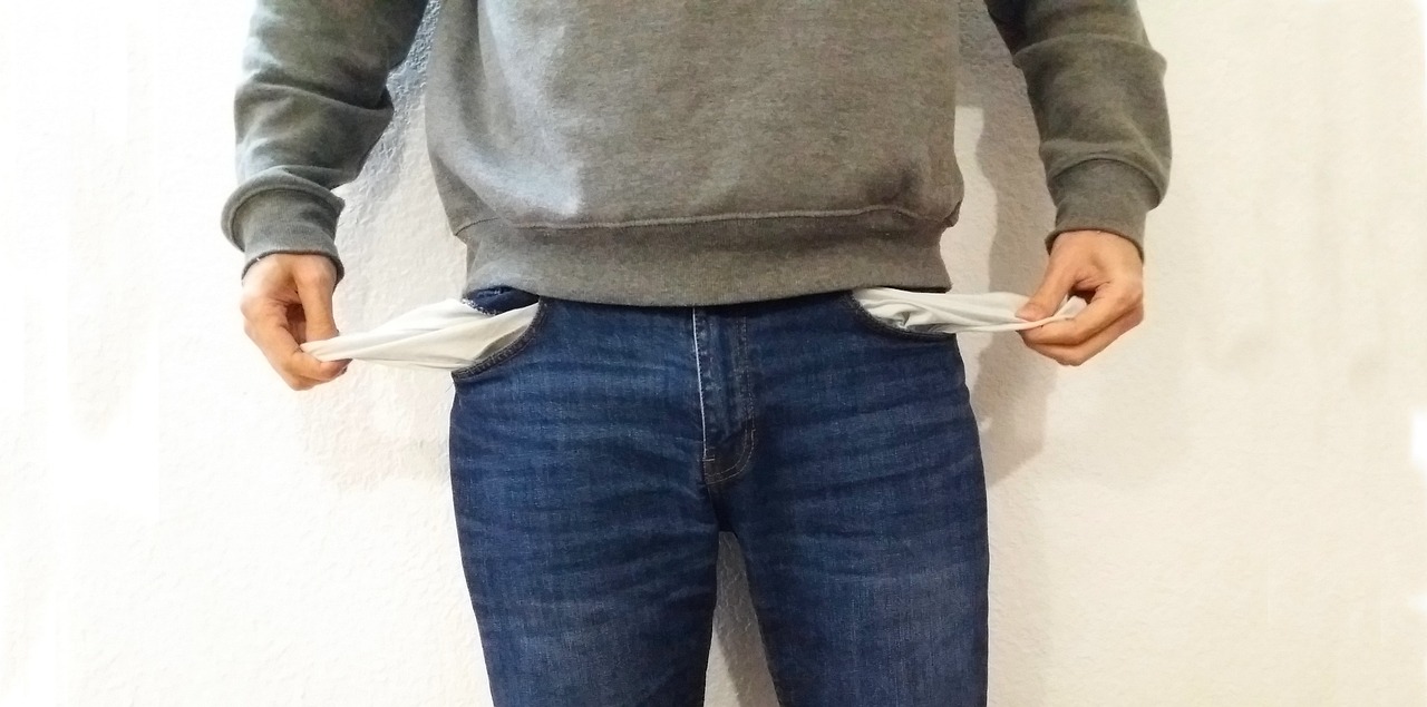 A young person in a hoodie playfully turning out both empty jeans pockets